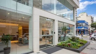 Fachada moderna de clínica com vidro, plantas na entrada e pessoas no interior em Florianópolis.