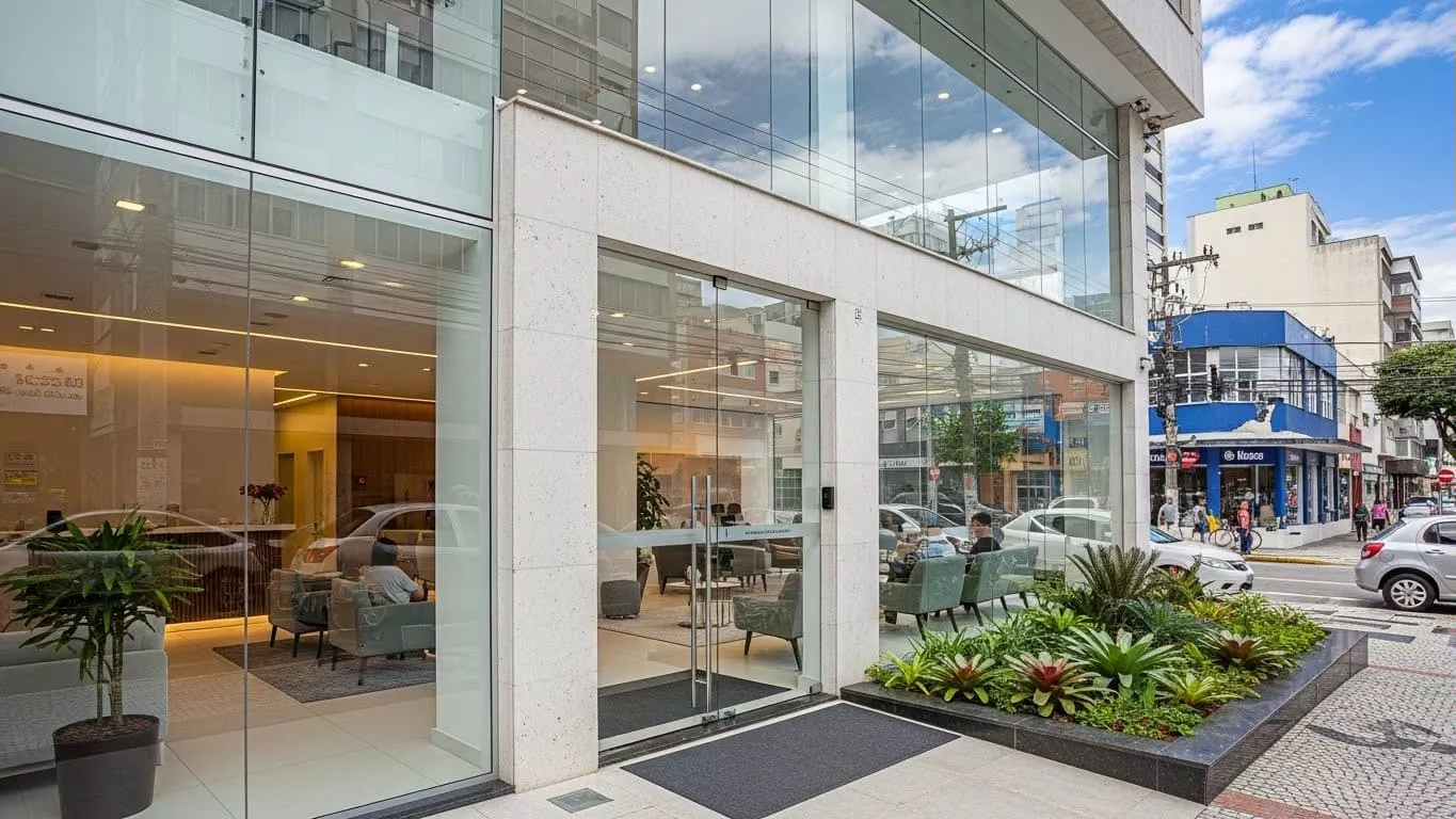 Fachada moderna de clínica com vidro, plantas na entrada e pessoas no interior em Florianópolis.