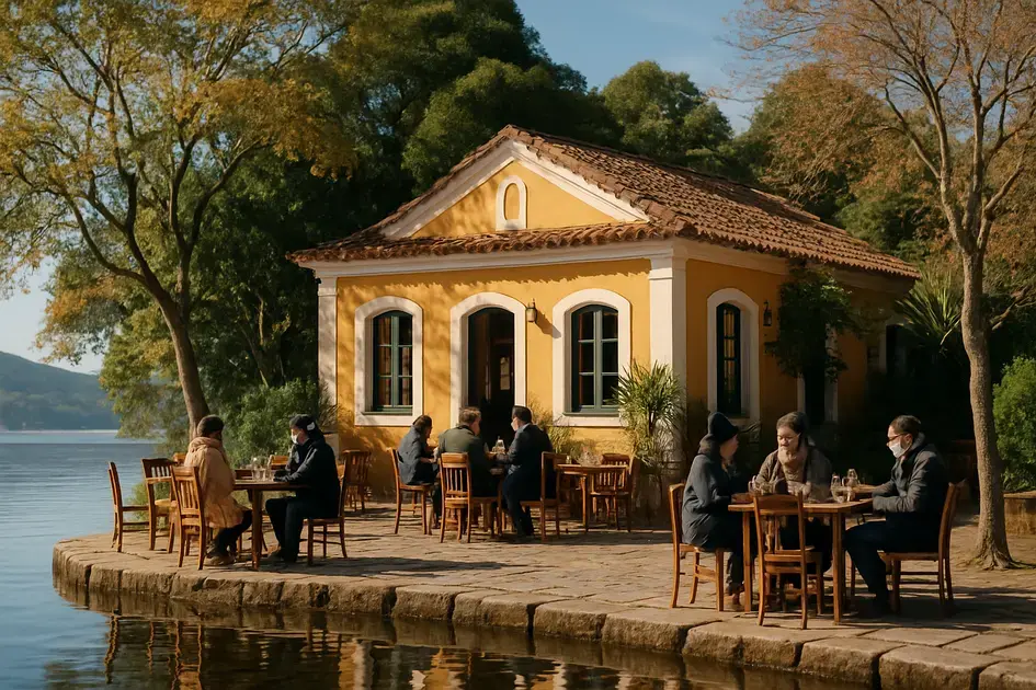 Casa amarela à beira do lago, com pessoas sentadas em mesas de madeira, rodeada por árvores no inverno.