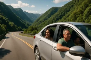 Carro em movimento na estrada, com montanhas verdes ao fundo e passageiros sorrindo dentro do veículo.