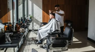 Barbearia moderna com cadeiras de couro, barbear e cliente em ambiente iluminado por janelas amplas.