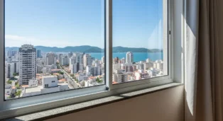 Vista panorâmica de Florianópolis com prédios e mar ao fundo, através de uma janela de esquadria de alumínio.
