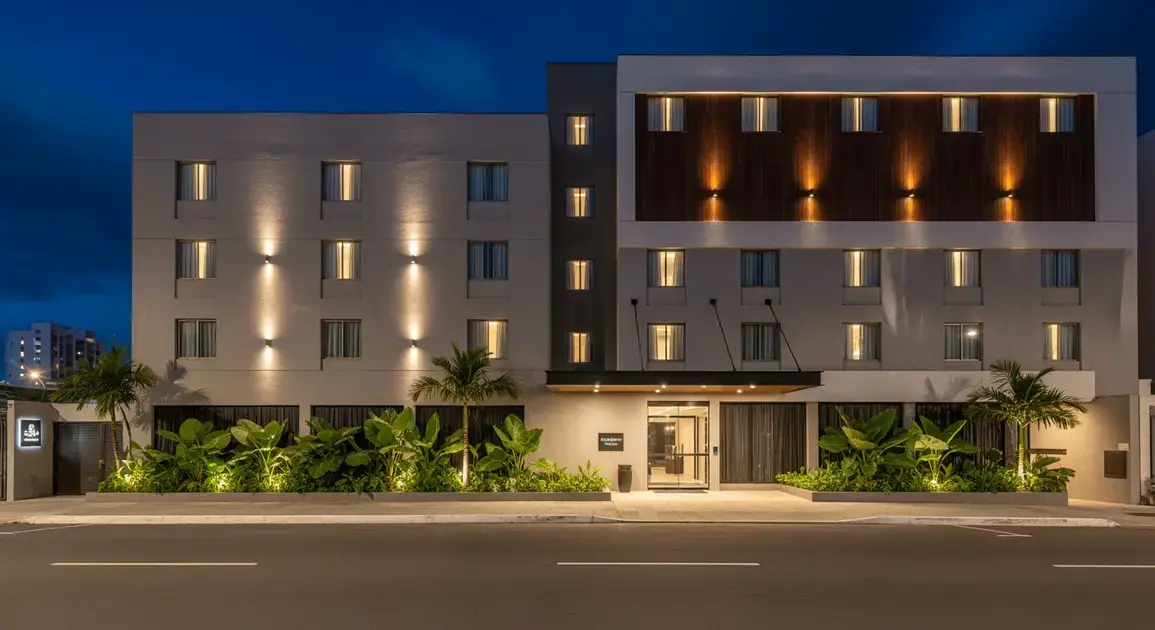 Fachada moderna de hotel iluminada à noite, com plantas na entrada e janelas amplas.