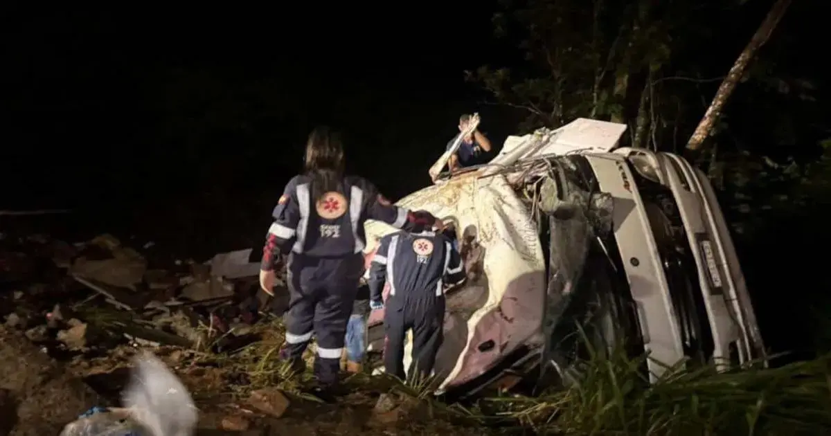 Caminhão capotado em área rural, com equipes de resgate trabalhando na cena à noite.
