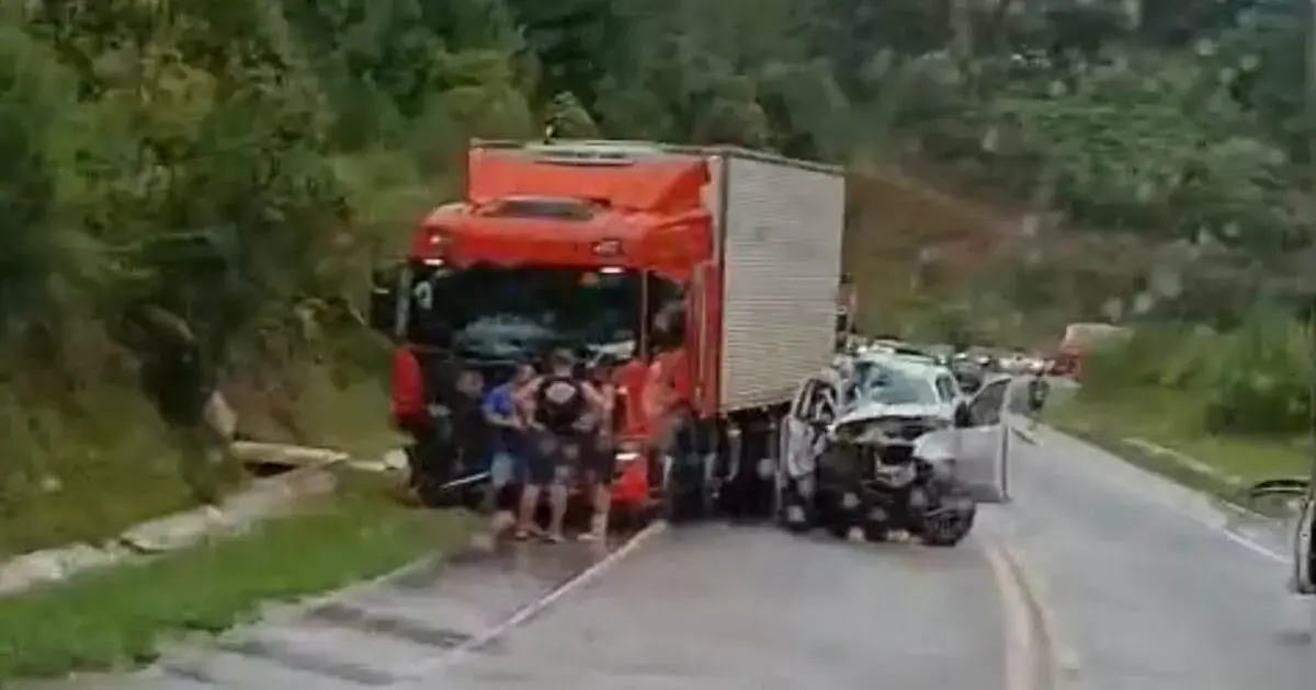 Caminhão vermelho colidido na BR-282 com carro danificado, pessoas ao redor avaliando a situação.