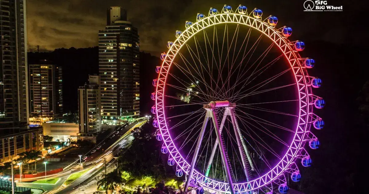Roda-gigante iluminada em Balneário Camboriú, cercada por prédios e com céu noturno.