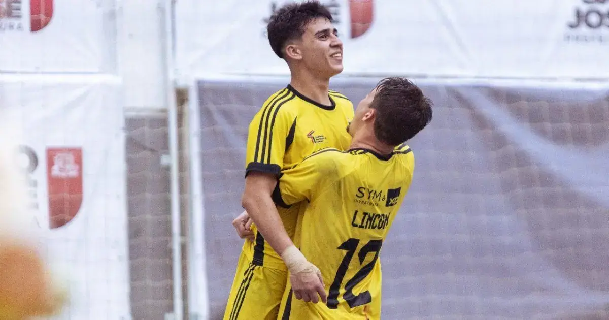 Dois jogadores de futsal comemoram um gol, vestindo uniformes amarelos, em um ginásio esportivo.