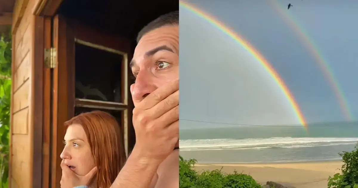 Casal surpreso observando um arco-íris duplo sobre o mar na Praia da Solidão, em Florianópolis.