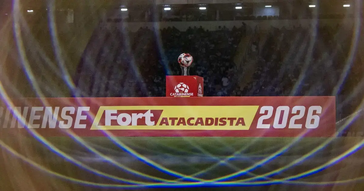 Troféu da Taça Acesc em destaque, com fundo de torcida e iluminação em campo de futebol.