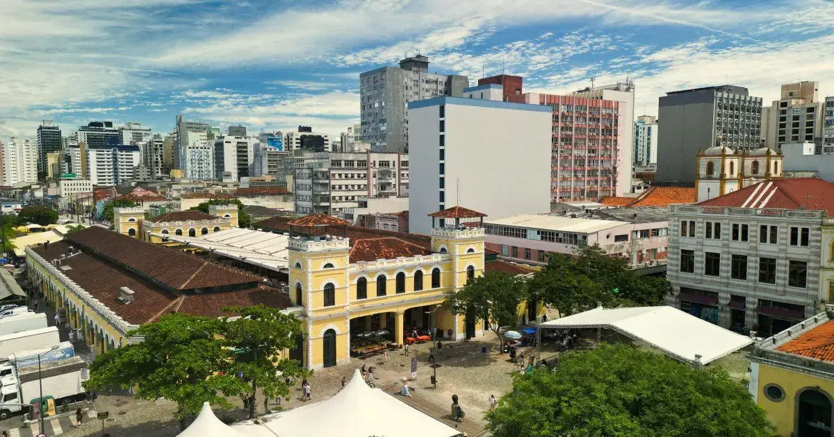 Vista aérea do centro de Florianópolis com prédios altos, céu azul e nuvens, e o Mercado Público em destaque.