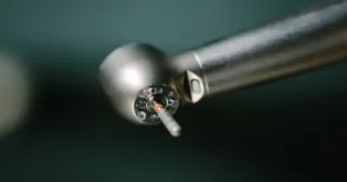 Broca cirúrgica de dentista com detalhe em metal e ponta visível, sobre fundo desfocado.