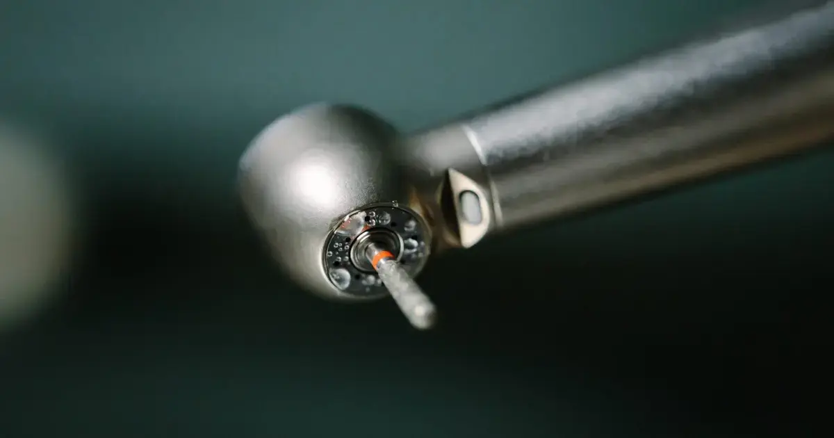 Broca cirúrgica de dentista com detalhe em metal e ponta visível, sobre fundo desfocado.