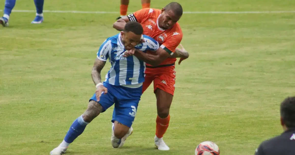 Jogadores do Avaí e Camboriú disputando a bola em campo, um jogador em azul caindo e outro em laranja segurando-o.