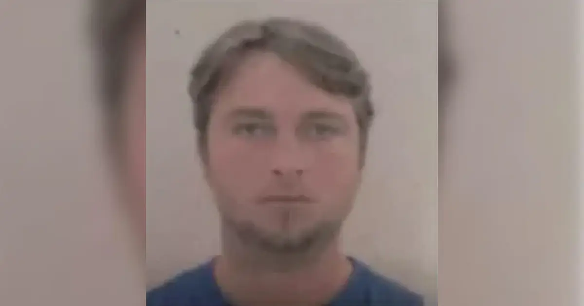 Homem com cabelo castanho claro e camiseta azul, olhando para a câmera em fundo neutro.