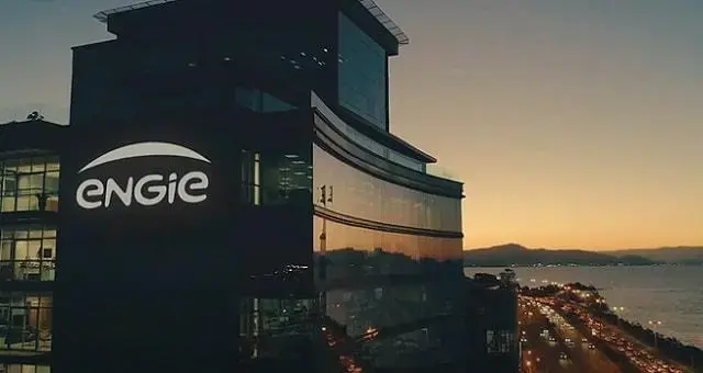 Prédio da ENGIE Brasil Energia com logo iluminado ao entardecer, vista da cidade e estrada ao fundo.