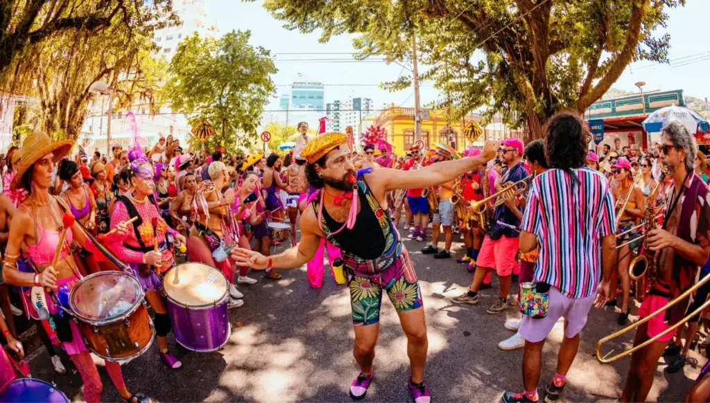 Grupo de foliões coloridos dançando e tocando instrumentos em rua de Florianópolis durante o Carnaval.