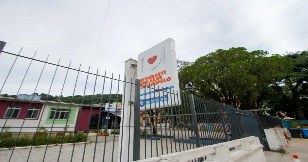 Fachada do Restaurante Popular em Florianópolis, com grade de proteção e árvores ao fundo.