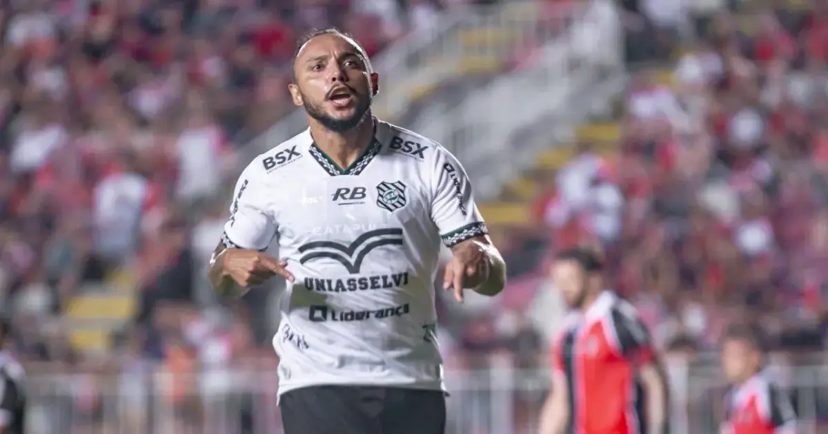 Jogador de futebol com uniforme branco e preto, gesticulando em campo durante uma partida.