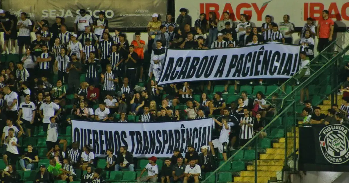 Torcida do Figueirense em estádio, segurando faixas com mensagens sobre paciência e transparência.