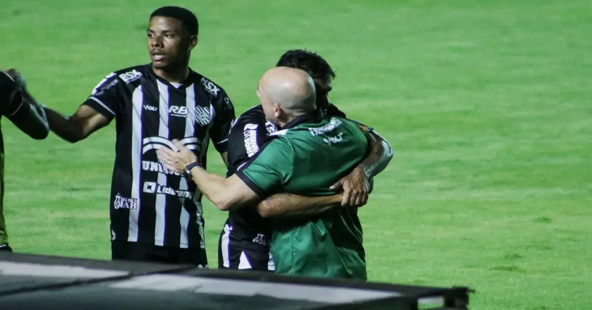Jogadores do Figueirense se abraçando em campo, com uniformes listrados em preto e branco, em clima de celebração.