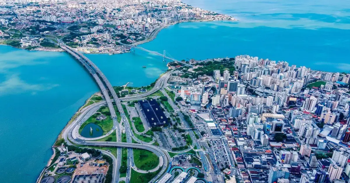 Vista aérea de Florianópolis, com a cidade, ponte e mar azul ao fundo.