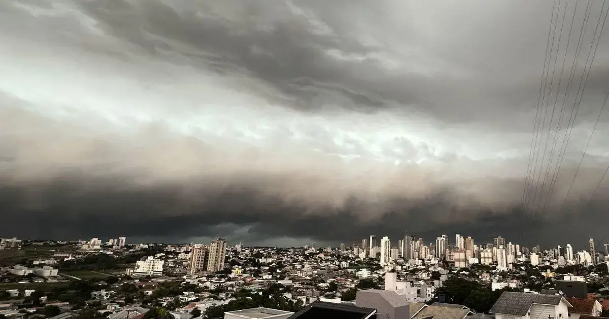 Nuvens escuras e ameaçadoras cobrem a cidade, com prédios visíveis ao fundo.