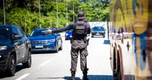 Guarda municipal orientando o tráfego em rua com veículos e vegetação ao fundo.
