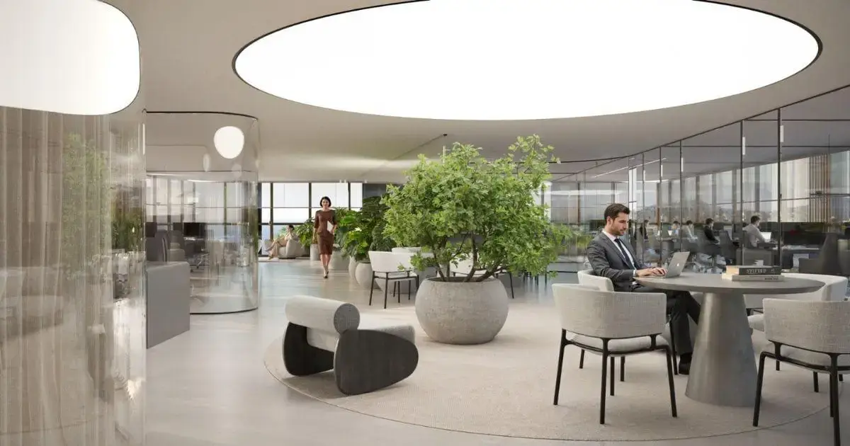 Ambiente moderno com plantas, mesas e cadeiras, pessoas trabalhando e iluminação circular no teto.