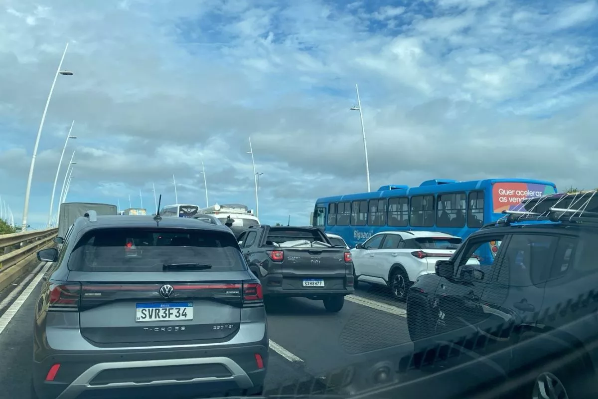 Trânsito parado com vários carros e um ônibus azul na Ponte Colombo Salles, céu nublado ao fundo.