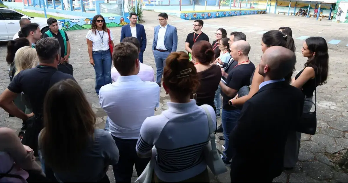 Grupo de pessoas em círculo, algumas conversando, em ambiente externo com mural colorido ao fundo.