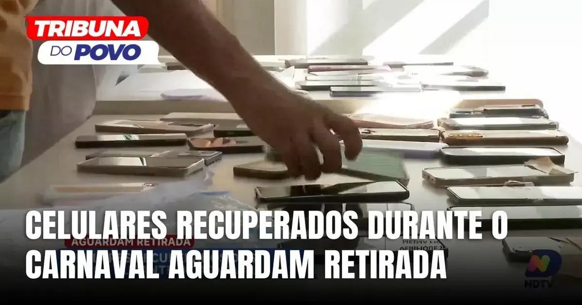 Celulares recuperados em mesa, com mão de pessoa selecionando um deles, em ambiente iluminado.