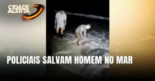 Policiais resgatam homem inconsciente na água, com ondas ao fundo e iluminação noturna na Praia dos Ingleses.