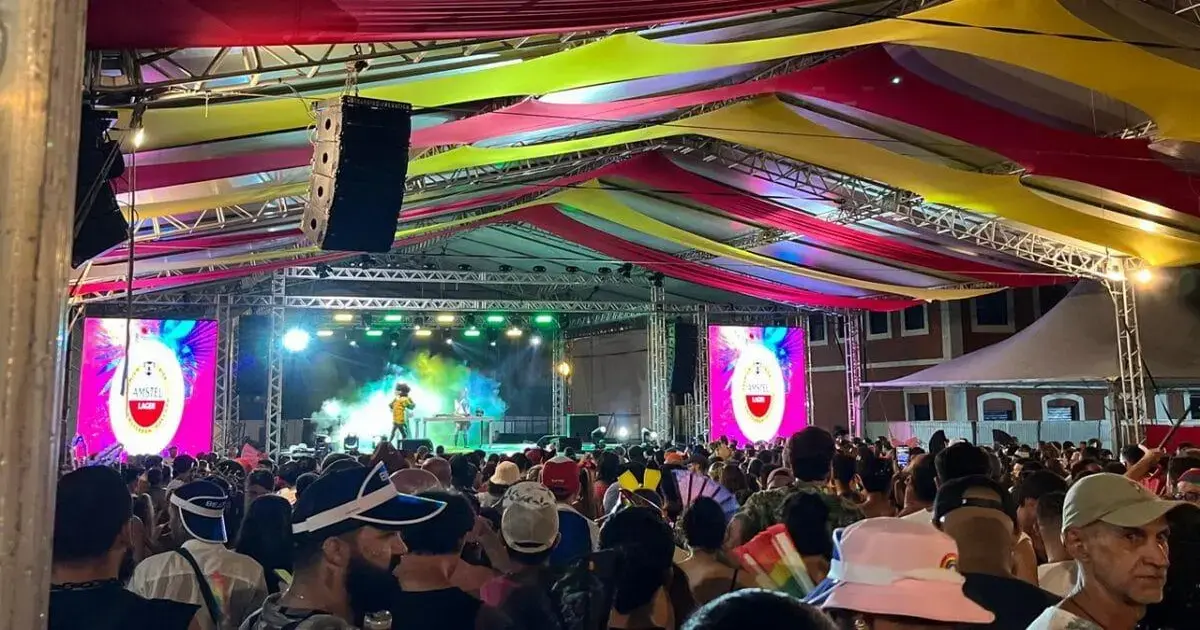 Multidão em evento no Centro de Florianópolis, com decoração colorida e palco iluminado ao fundo.