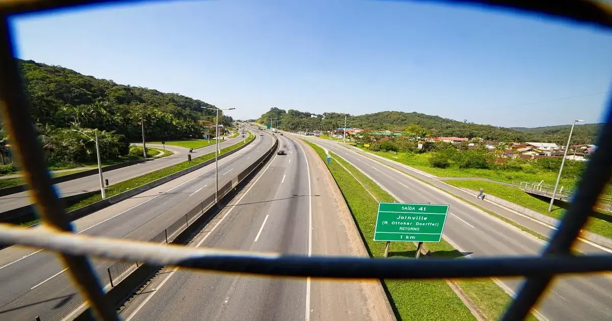 Vista da BR-101 Norte com sinalização para Joinville, vegetação ao fundo e pista vazia.