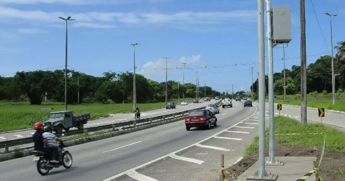 Radares de velocidade instalados em rodovia com veículos em movimento e vegetação ao fundo.