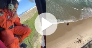 Helicóptero de resgate sobrevoando a Praia da Joaquina, com vista para a areia e o mar.