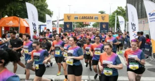 Participantes da corrida Chão da Cidade cruzam a linha de largada em um evento esportivo movimentado.