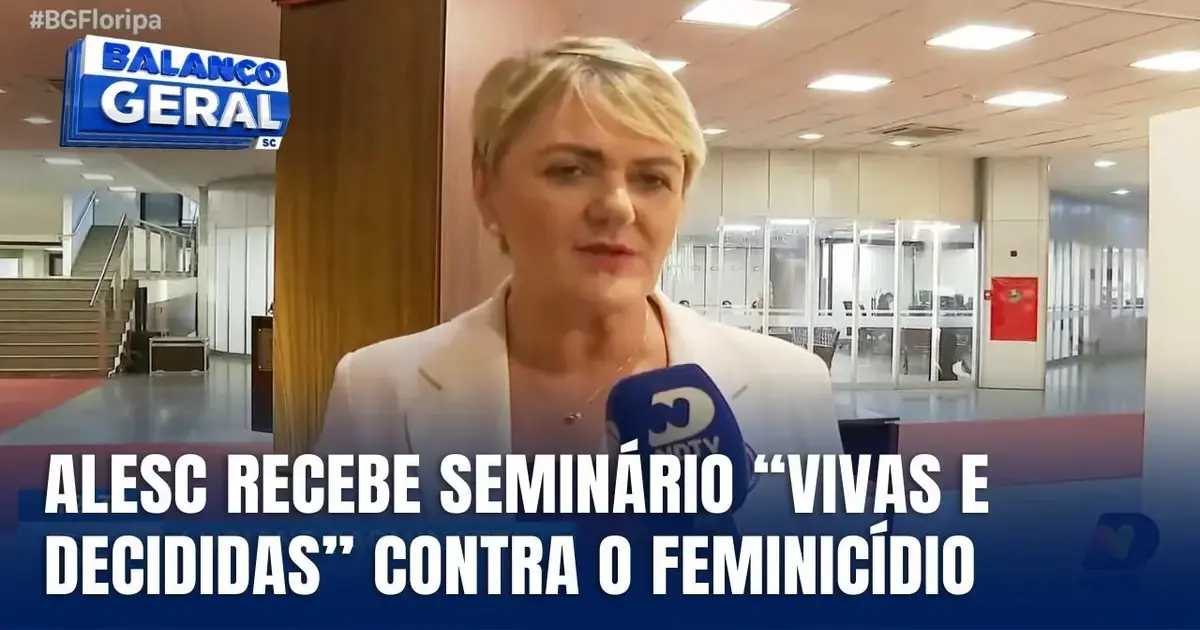 Mulher em ambiente interno, falando ao microfone, com painel informativo ao fundo sobre seminário contra feminicídio.
