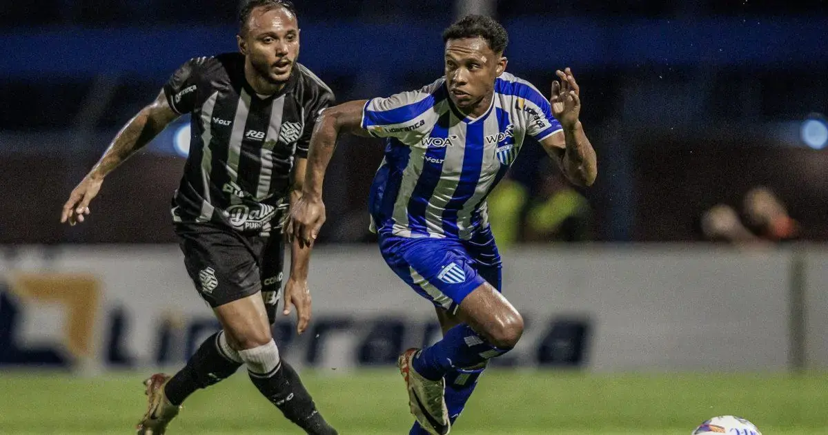 Dois jogadores de futebol em ação durante uma partida, um em uniforme listrado preto e o outro em azul e branco.