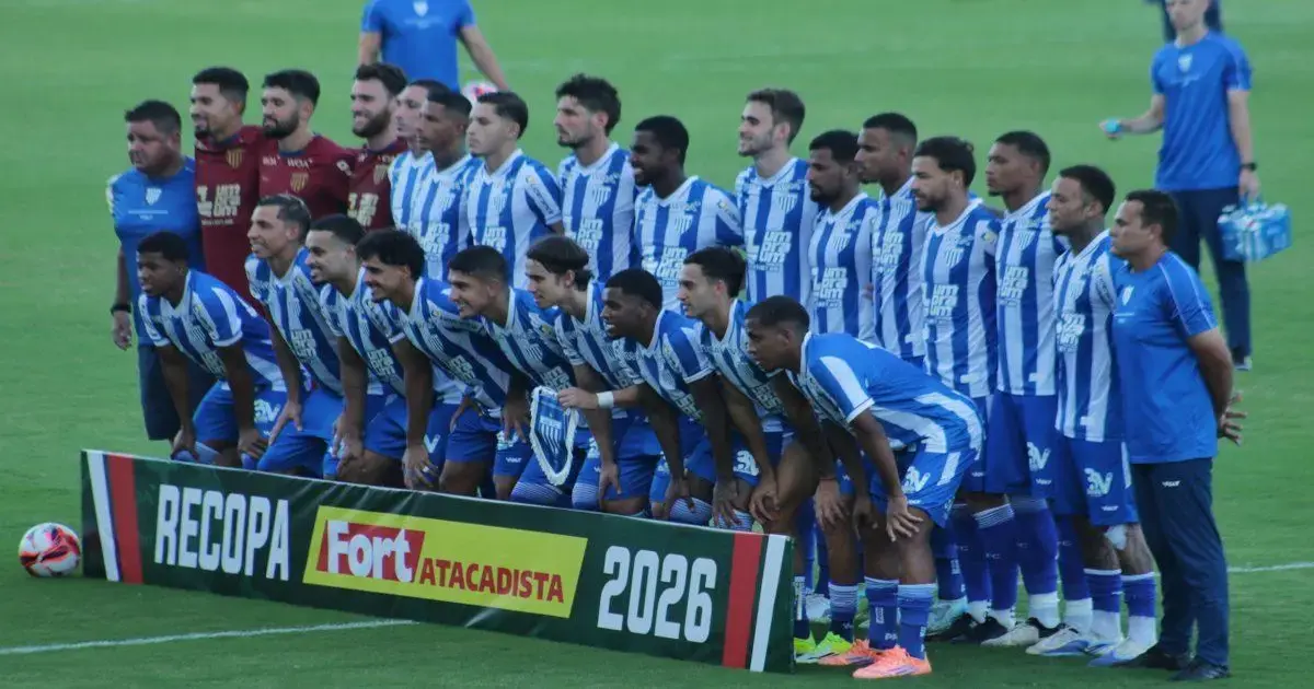 Elenco de time de futebol posando em campo com faixa escrito 