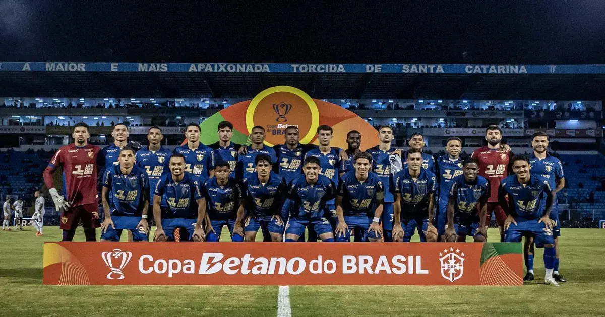 Time posado em campo com uniforme azul e amarelo, em frente a um painel da Copa Betano do Brasil.