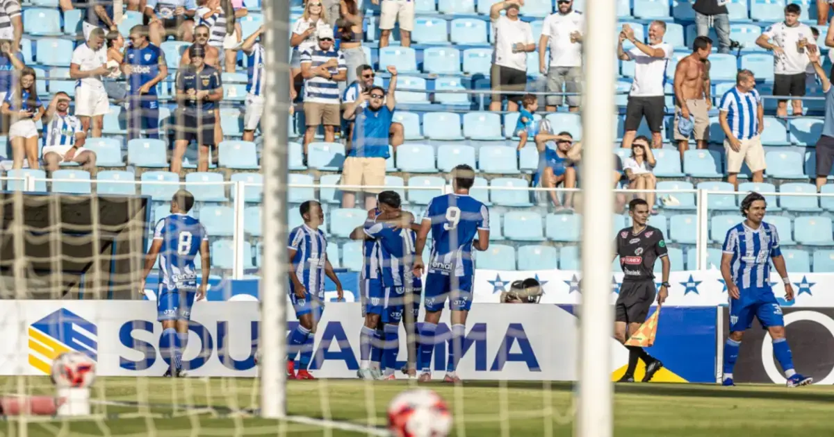 Jogadores comemoram após um gol em um jogo de futebol, com torcedores ao fundo.