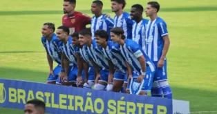 Jogadores de futebol alinhados em pose de foto, com uniforme azul e branco, em campo, em frente a um banner com texto.