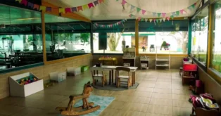 Espaço interno com mesas e cadeiras, brinquedos coloridos e decoração festiva em uma sala infantil.