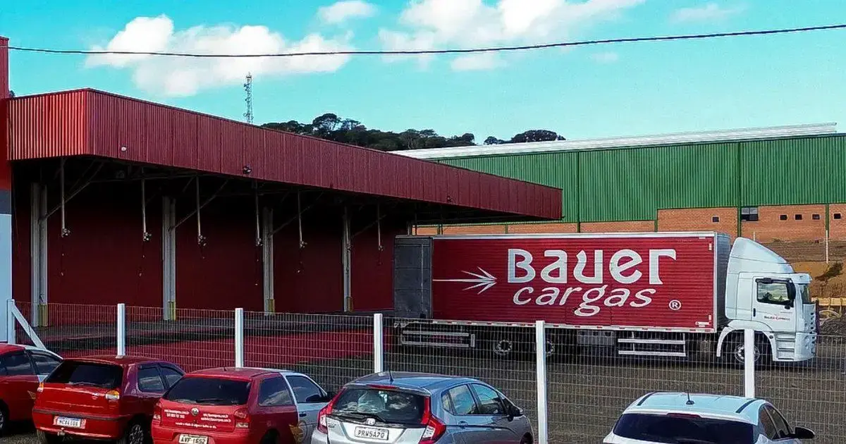 Caminhão da Bauer Cargas estacionado em frente a um galpão, com vários carros ao redor.