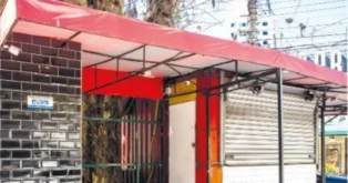 Quiosque com teto vermelho, estrutura metálica, parede de ladrilho preto e fechamento em rolo metálico.