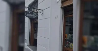 Placa com o nome "Sorrentino Café & Doces" na fachada de um estabelecimento em rua com paredes brancas.