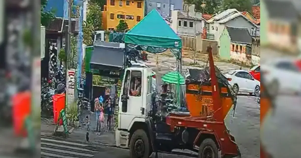 Caminhão de lixo estacionado em uma rua, sob uma tenda, com pessoas e bicicletas ao redor.