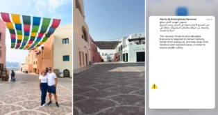 Casal posando em área urbana com prédios coloridos e bandeirinhas penduradas, fundo com vista da cidade. Texto de alerta de emergência à direita.