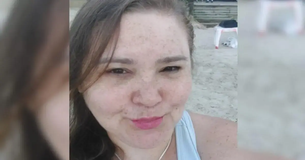 Primeiro plano de uma pessoa sorrindo, com pele clara e cabelo castanho, em uma praia.